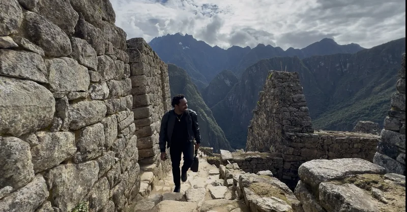 Bakari Akil at Machu Picchu, Peru Bakari Akil walking through the ancient stone ruins of Machu Picchu, Peru, dressed in all black, the Andes mountains and misty cloud forest dropping away behind the Inca citadel
