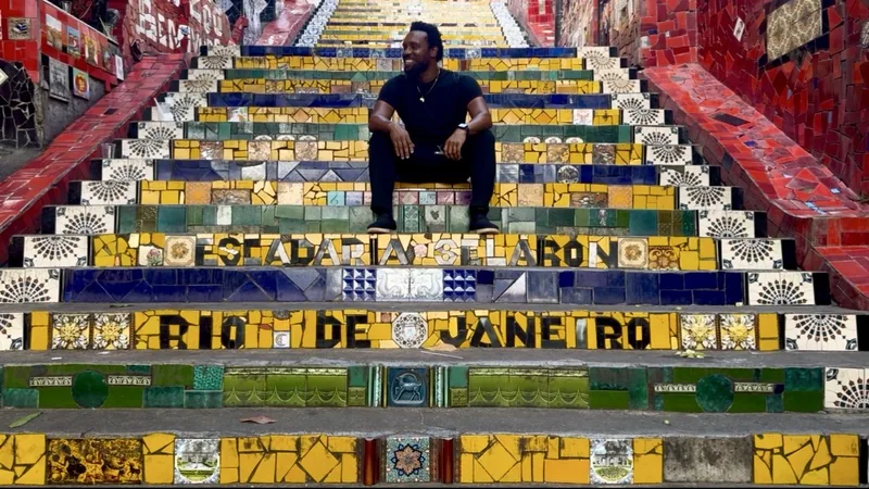 Bakari Akil at Escadaria Selarón, Rio de Janeiro, Brazil Bakari Akil standing on the colorful mosaic-tiled Escadaria Selarón steps in Rio de Janeiro, Brazil, tiles spelling out RIO DE JANEIRO in bright yellow, red, green, and blue around him